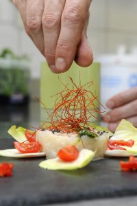 Hand eines Kochs streut Safranfäden auf sein Gericht