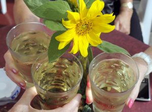 Hände dreier Menschen nehmen sich weinschorle von einem Tisch mit gelber Blume