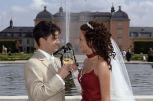 Hochzeitspaar pristet sich vor Springbrunnen und Schwetzinger Schloss mit Wein zu