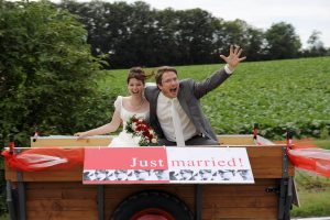 Feierndes Hochzeitspaar auf Anhänger mit Just Married Schild