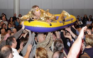 ganz in Gold gekleideter Sänger macht Crowdsurfing in einem Schlauchboot