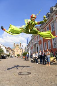 Stelzenläufer im Spagatsprung vor Speyerer Dom und Rathaus