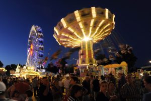 Sich rasant drehendes Kettenkaussell und Riesenrad über abendlichen Brezelfestbesuchern