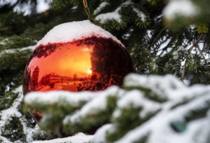 In einer roten Christbaumkugel, die an einem schneebedeckten Baum hängt, spiegelt sich der verschneite Domplatz