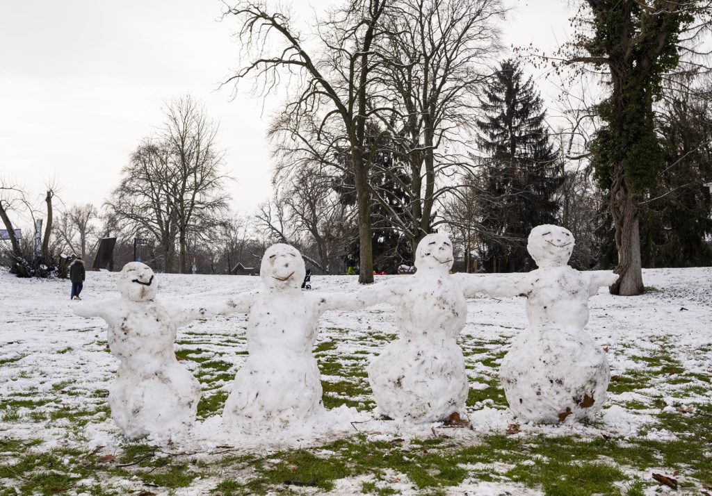 Vier lachende Schneemänner stehen sich an den Händen haltend in einer Reihe auf der verschneiten Domwiese