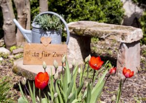 Steinbank in Garten mit Gießkanne und Schild "Ein Platz für Zwei"