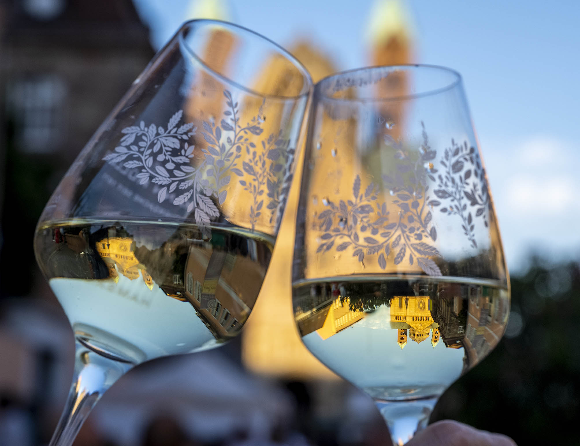 Zwei Gläser mit Weißwein und Blätterdekor stoßen an, im Hintergrund verschwommen der Speyerer Dom, der sich kopfüber in Wein spiegelt
