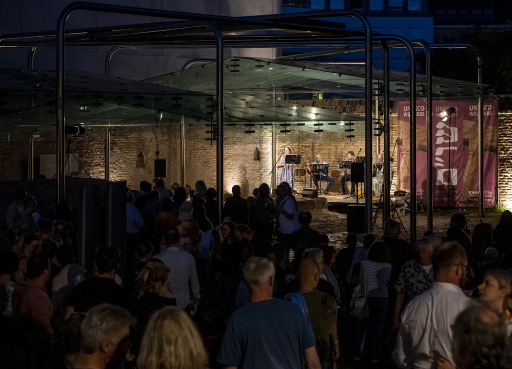 Das Publikum drängt sich im Judenhof an der Mikwe, im Hintergrund die Bühne mit den Musikern