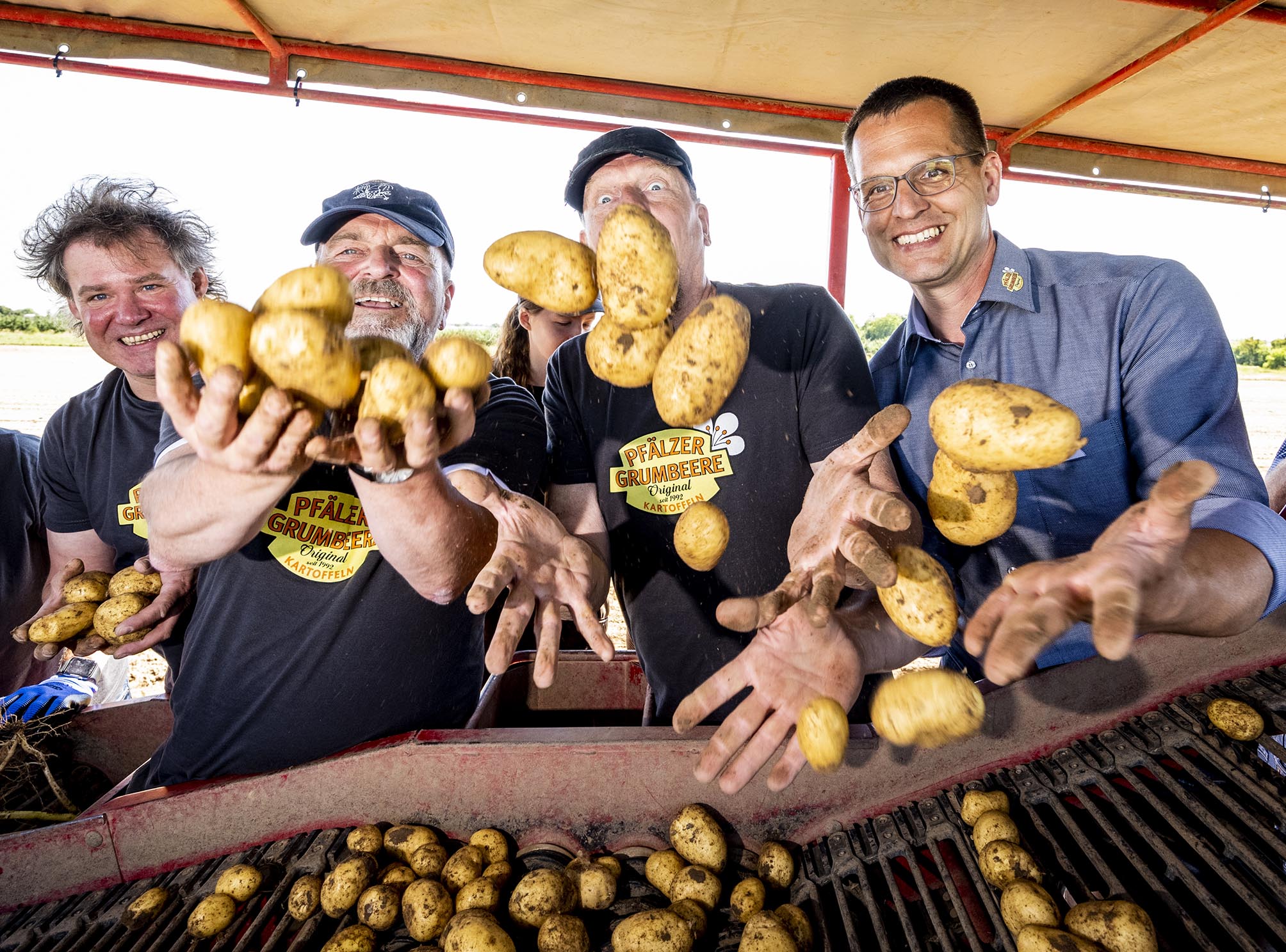 Sänger Edsel und Schlagzeuger Stefan Brod werfen mit dem Vorsitzenden der Erzeugergemeinschaft Hartmut Magin auf der Erntemaschine sitzend Kartoffeln in die Kamera