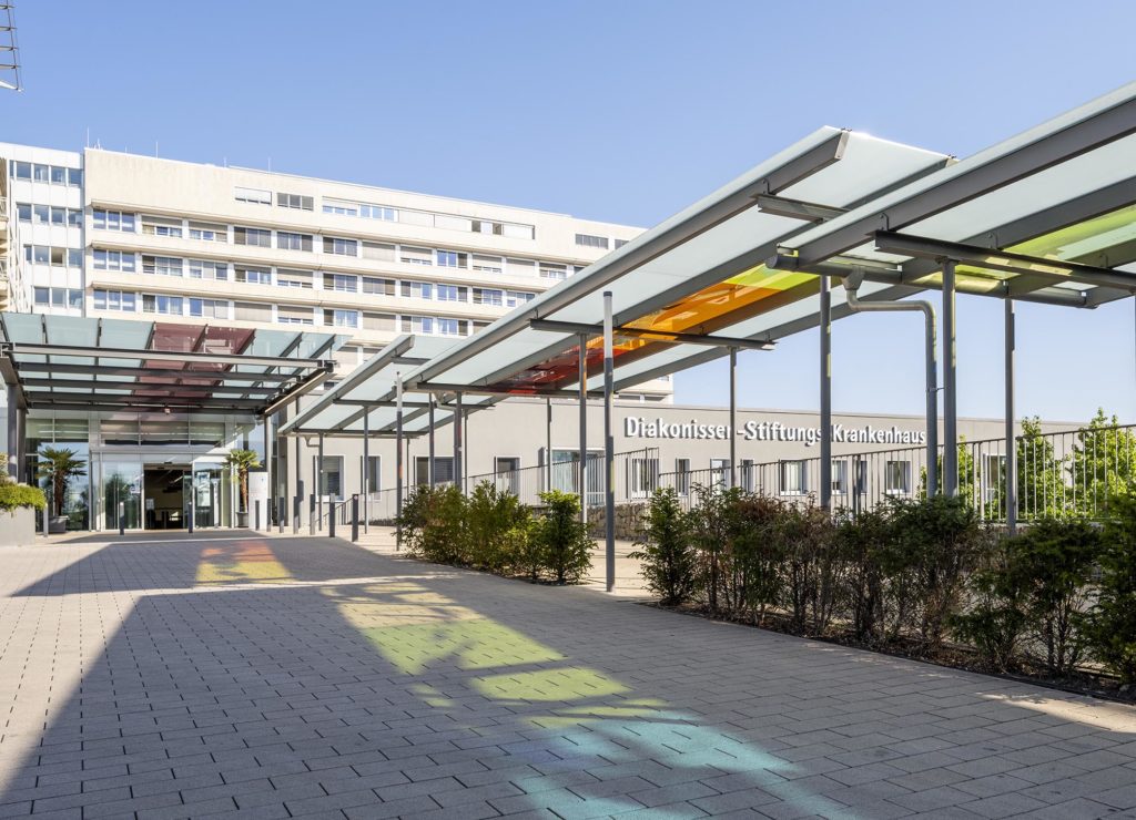 Bunte Lichteffekte in der Einfahrt zum Diakonissen-Krankenhaus Speyer durch die Sonnenstrahlen, die durch das bunte Glas über dem Fußweg fallen