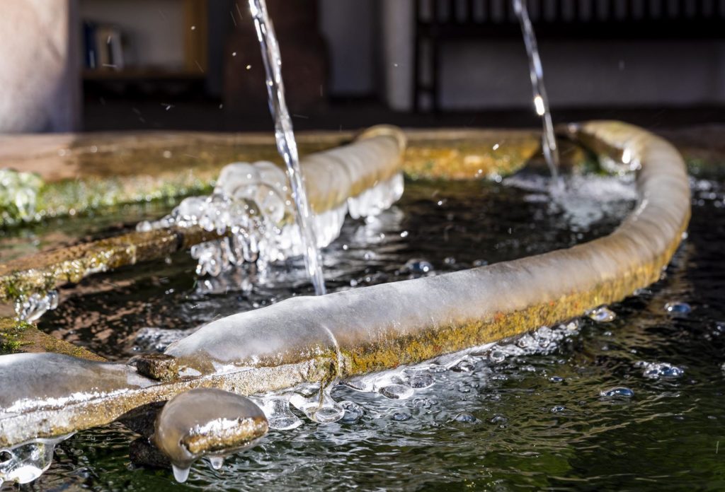 Nahaufnahme vereister Brunnen, in den von oben neues Wasser plätschert