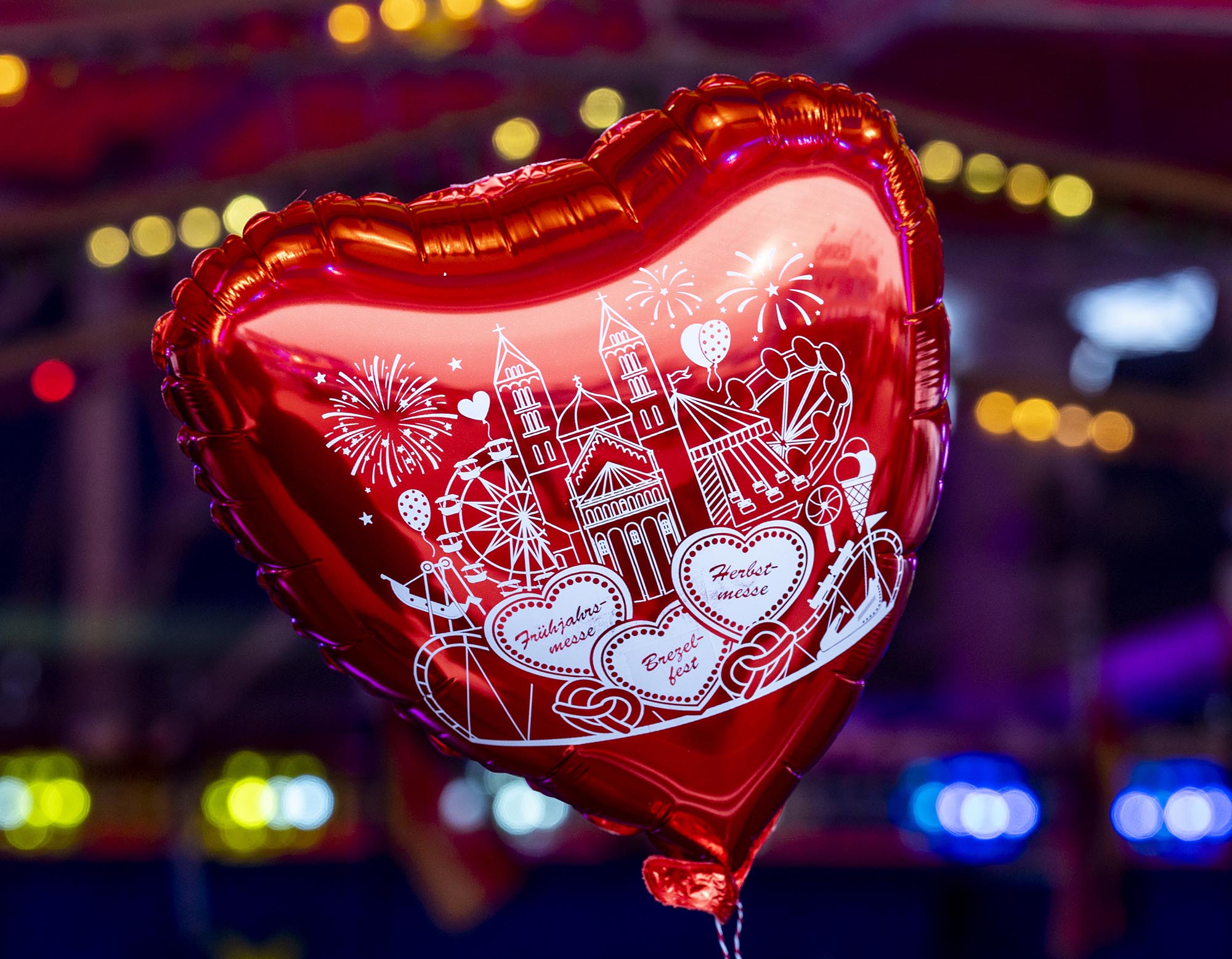 Herzförmiger roter Ballon mit einer Zeichnung des Speyerer Doms vor bunten Hintergrundlichtern