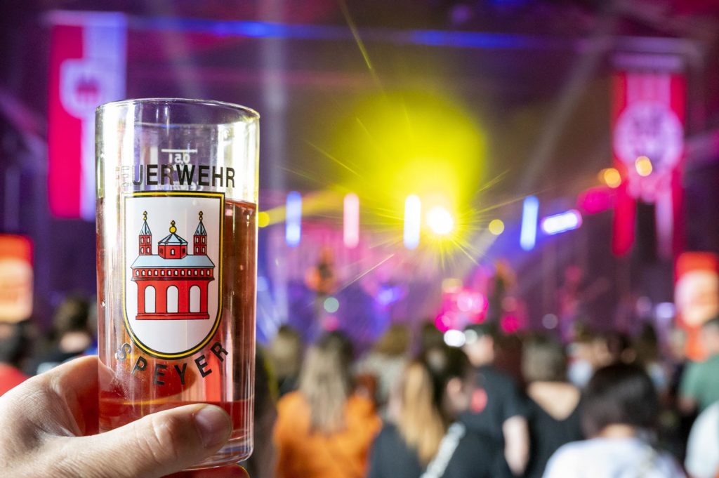 Weinschorle mit Feuerehrlogo mit Konzert im Hintergrund