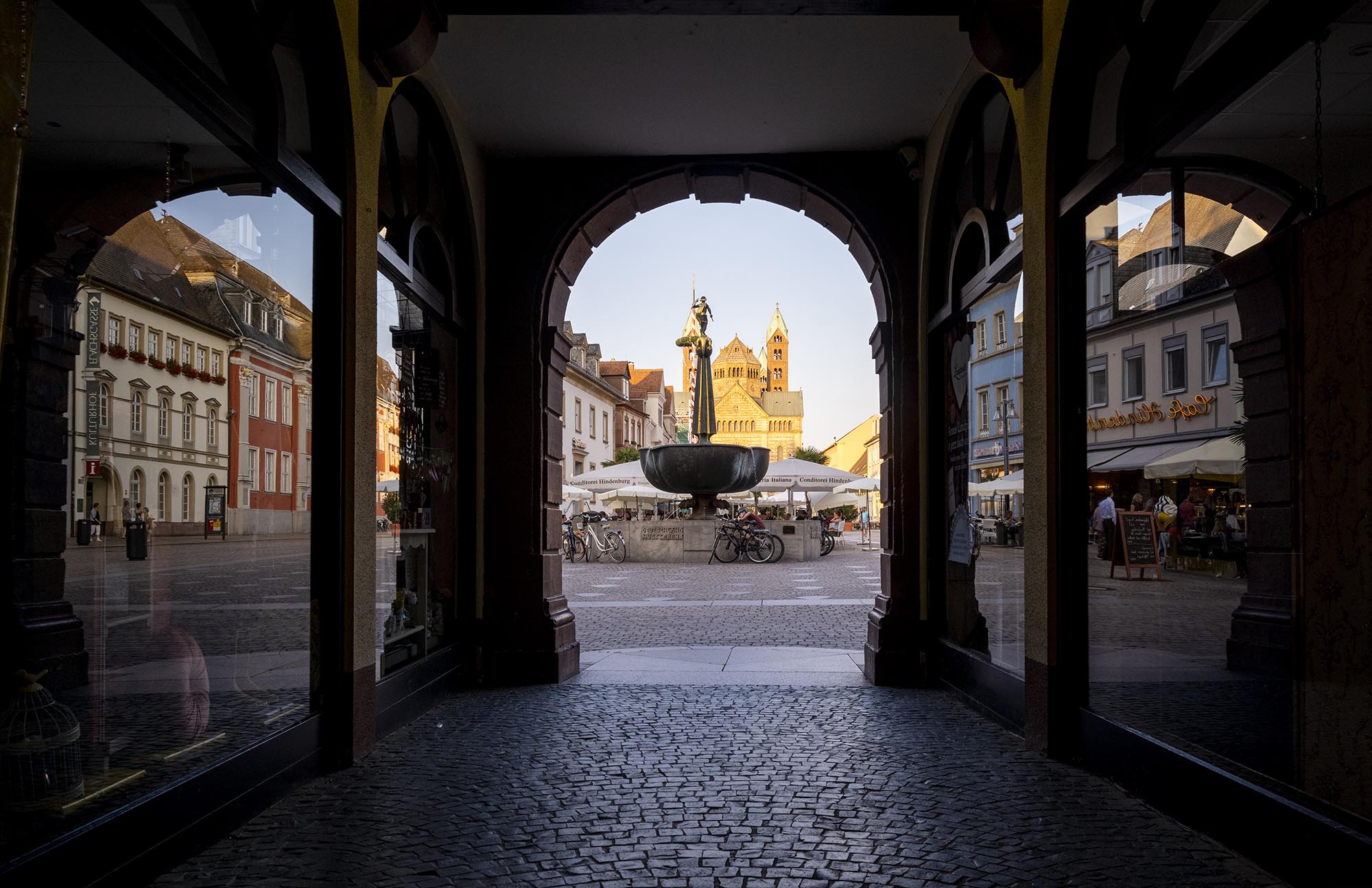 Blick in der Abenddämmerung durch die Arkade des Gebäudes Alte Münz auf den Platz vor dem Gebäude mit dem St. Georgsbrunnen. In den Schaufenstern der Geschäfte spiegeln sich historische Gebäude