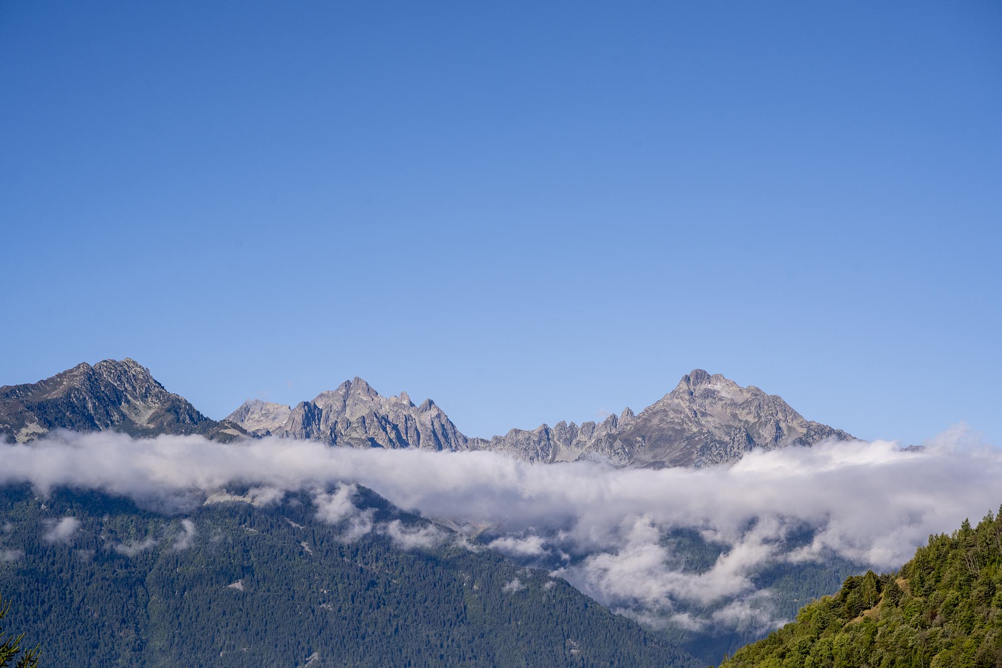 Wolkenverhangene Bergspitzen leuchten im Sonnenaufgang vor blauem Himmel