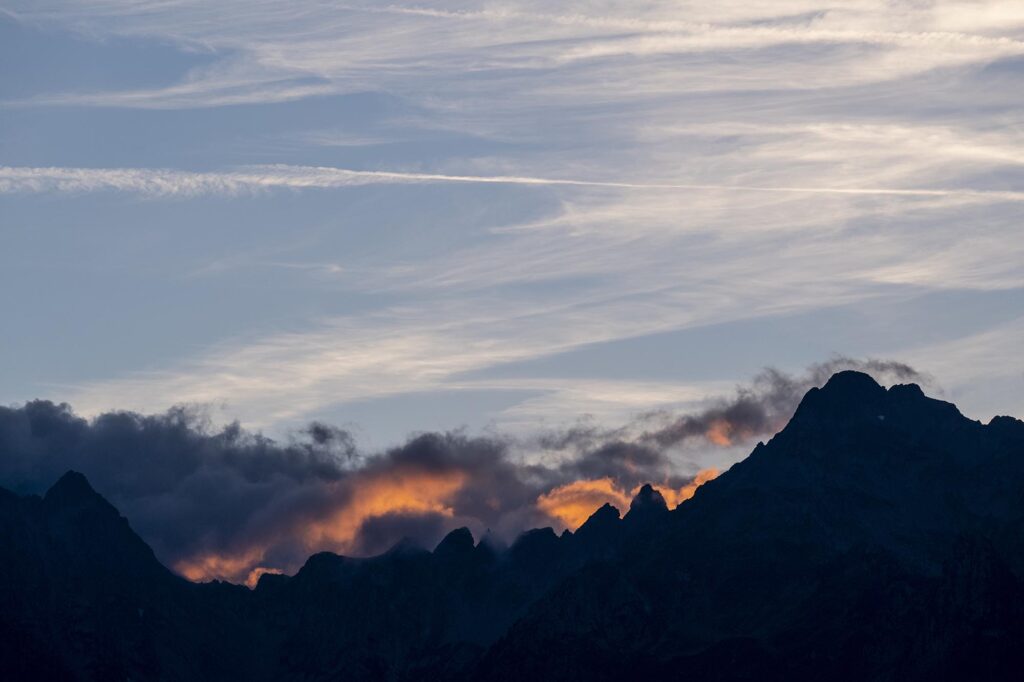 Sonnenuntergang mit dunklen Wolkenfetzen über Berggipfeln am Horizont