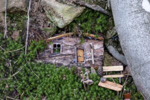 Minihausfassade aus Holz mit kleiner Bank und Tisch vor der Tür im grünen Pflanzenbewuchs zwischen Bäumen