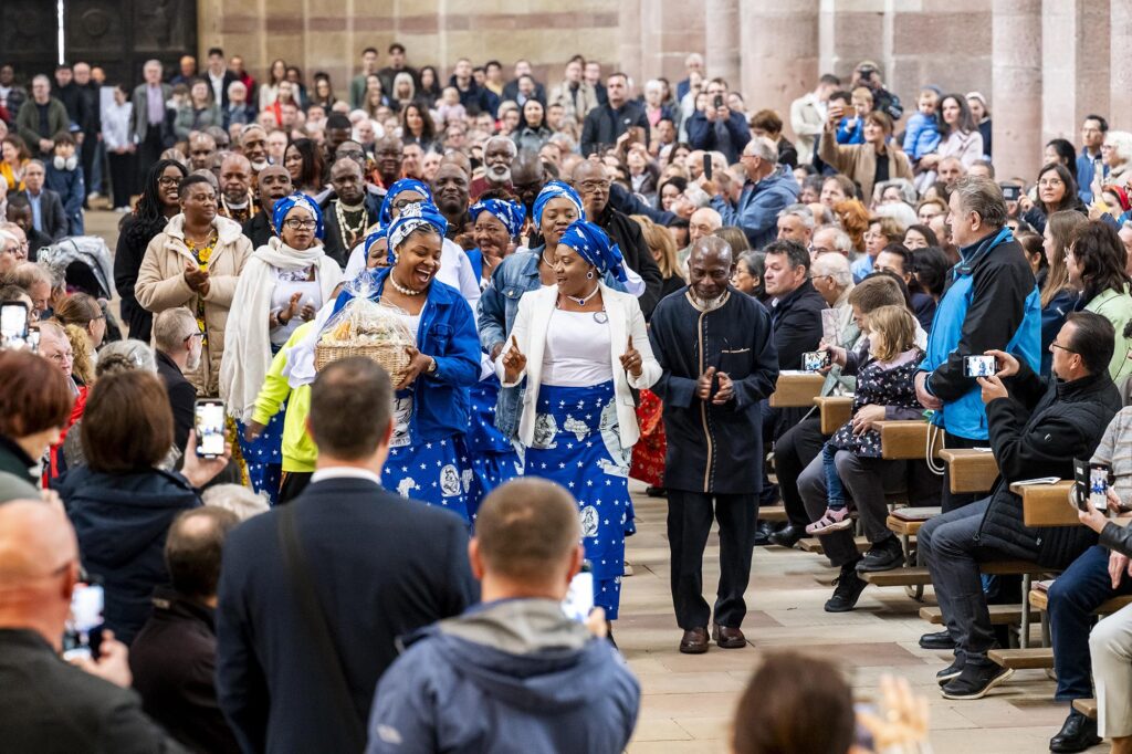 Die Gläubigen freuen sich über den singenden und tanzenden Eintritt der nigerianischen Gemeinde zur Gabenbereitung durch den Mittelgang zum Altar
