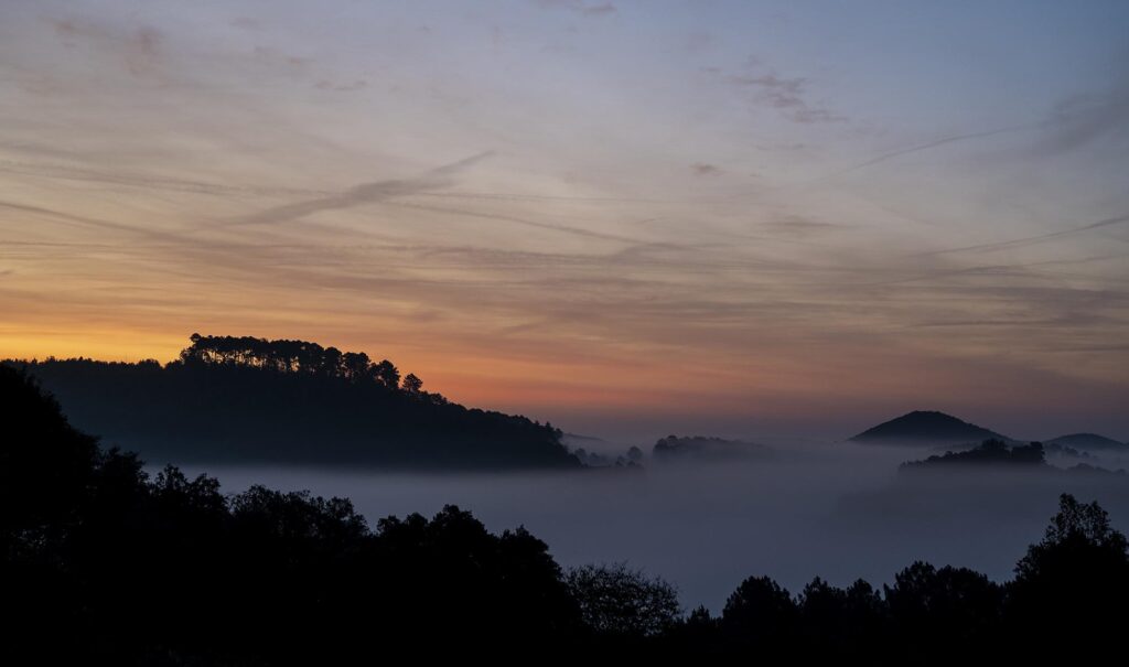 Sonnenaufgang über einer bewaldeten Berglandschaft mit Nebel zwischen den Gipfeln