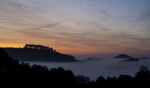 Sonnenaufgang über einer bewaldeten Berglandschaft mit Nebel zwischen den Gipfeln