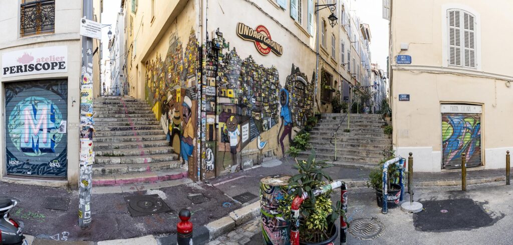Bunt bemalte Straßenecke zwischen zwei häusergesäumten Treppen die in verschiedenen Richtungen den Hügel hinauf führen.