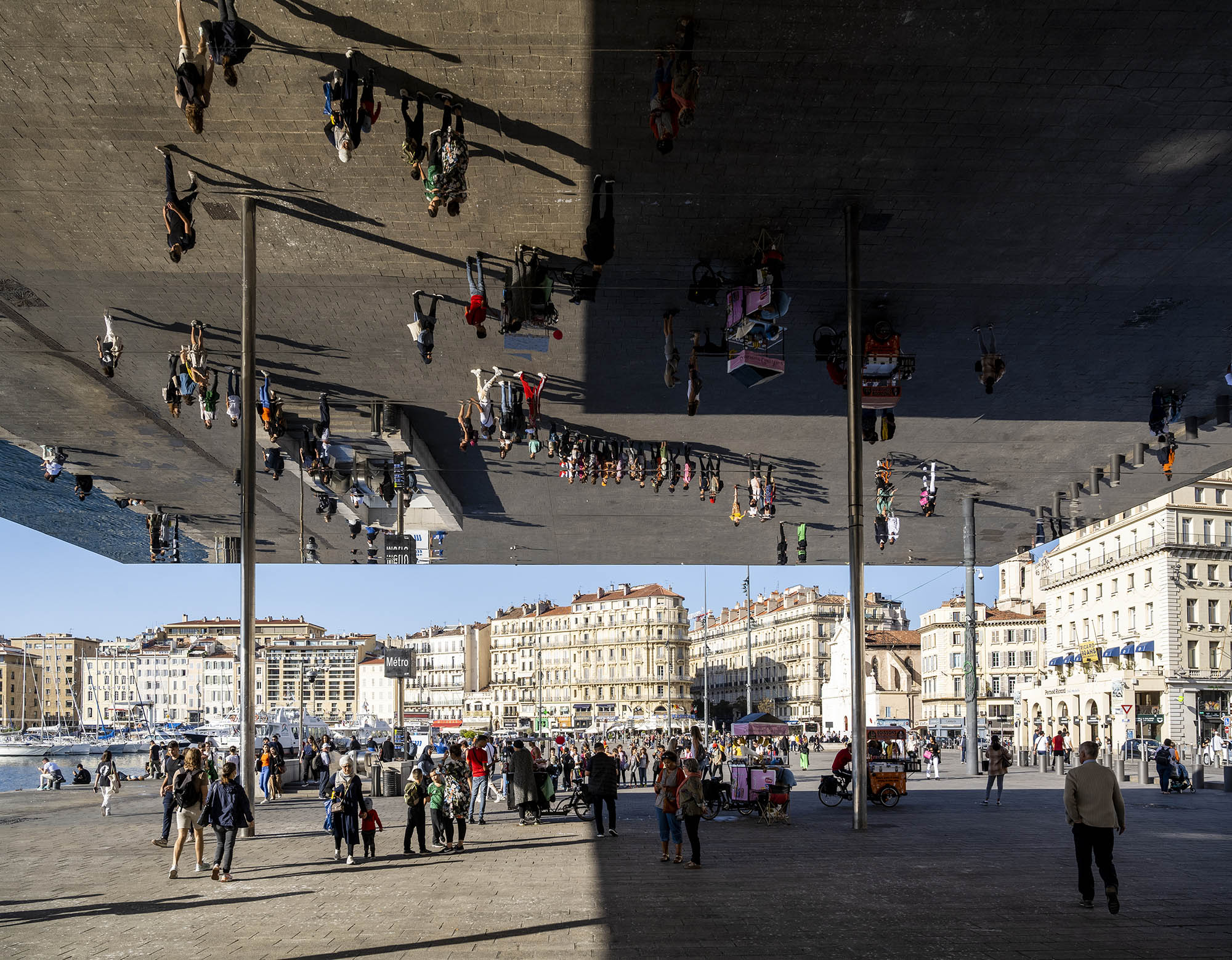 Menschen am Hafen von Marseille werden über Kopf in der Spiegelinstallation Ombrière de Norman Foster reflektiert