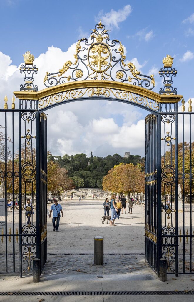 Eingang mit goldverziertem schmiedeeisernen Tor zum Jardin de La Fontaine in Nîmes