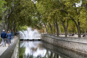 Blick entlang eines mit Bäumen umsäumten gemauerten Kanals mit Wasserfontäne