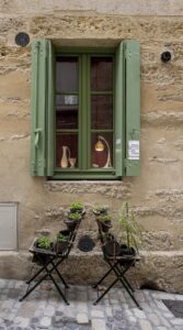 Grünes Fenster in Sandsteinhaus, davor zwei Stühle Rücken an Rücken mit Pflanzen