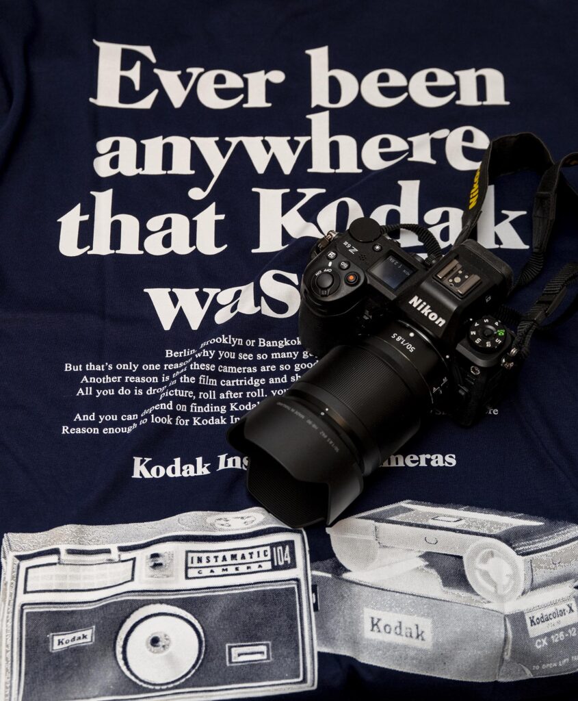 T-Shirt mit des Schriftzug „Ever been anywhere that Kodak wasn‘t?“. Auf dem T-Shirt liegt eine Kamera Nikon Z6 III mit aufgesetztem Objektiv Z 1,8/50 S