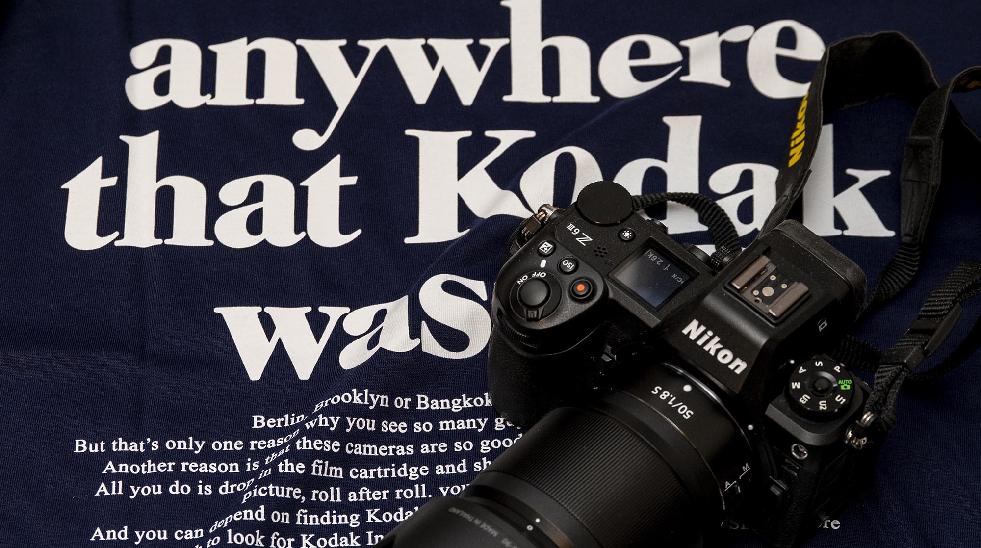 T-Shirt mit einem Schriftzug des ehemaligen Filmherstellers Kodak. Auf dem T-Shirt liegt eine Kamera Nikon Z6 III mit aufgesetztem Objektiv Z 1,8/50 S