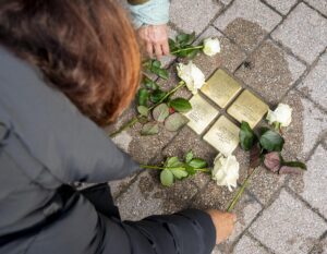 Menschen legen weiße Rosen zu den Stolpersteinen