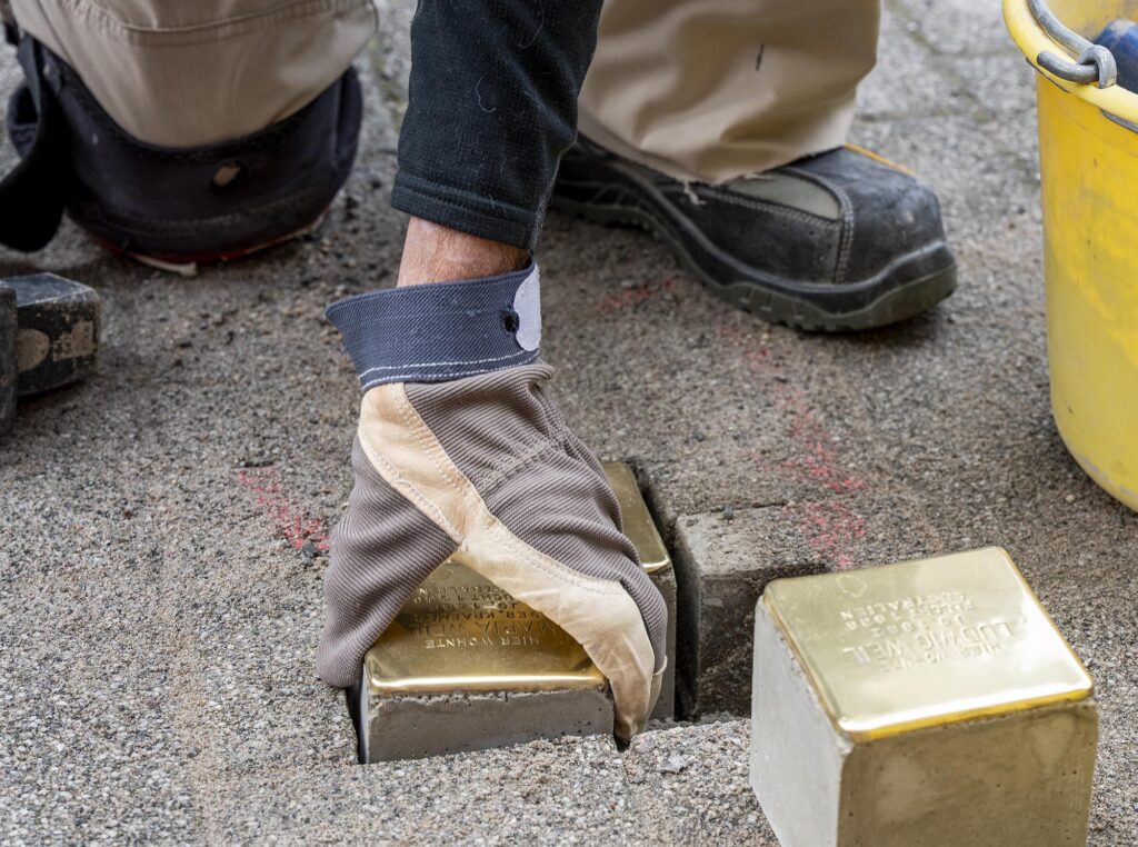 Großaufnahme einer Hand im Arbeitshandschuh, die gerade einen Stolperstein ins Pflaster setzt.