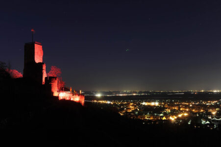 Rot beleuchtete Burgruine Wachtenburg bei Nach mit Blick über das erleuchtete Wachenheim